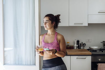 Calm hispanic sportswoman with phone and juice in kitchen