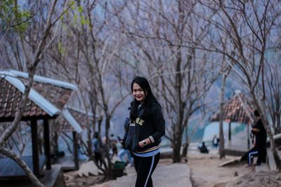 Portrait of smiling woman standing against bare trees during winter