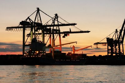 Silhouette cranes at harbor against clear sky