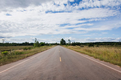 Empty road amidst field against sky