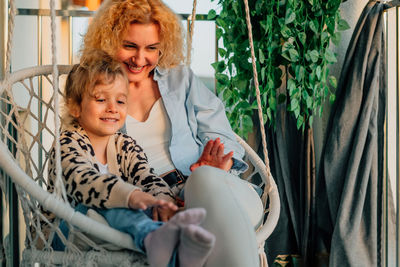 Close-up portrait happy mother with daughter at home on the balcony sitting in a hammock chair