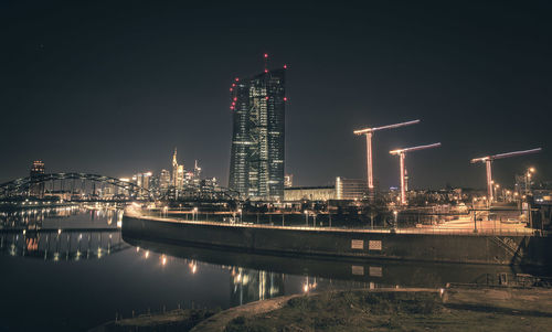 Illuminated buildings by river against sky at night