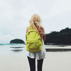 Rear view of woman carrying backpack at beach against sky