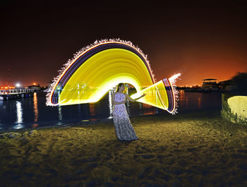 Illuminated ferris wheel on beach against sky at night
