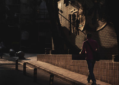 Rear view of man walking on footpath against buildings in city
