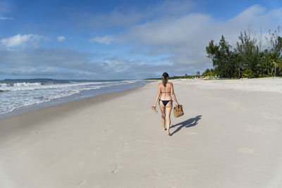 Rear view of woman walking at beach against sky