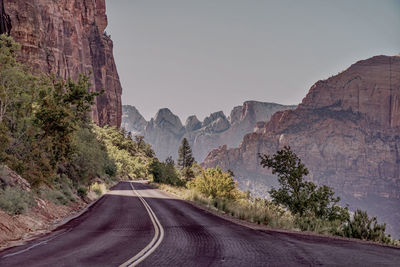 Road amidst trees and mountains against sky