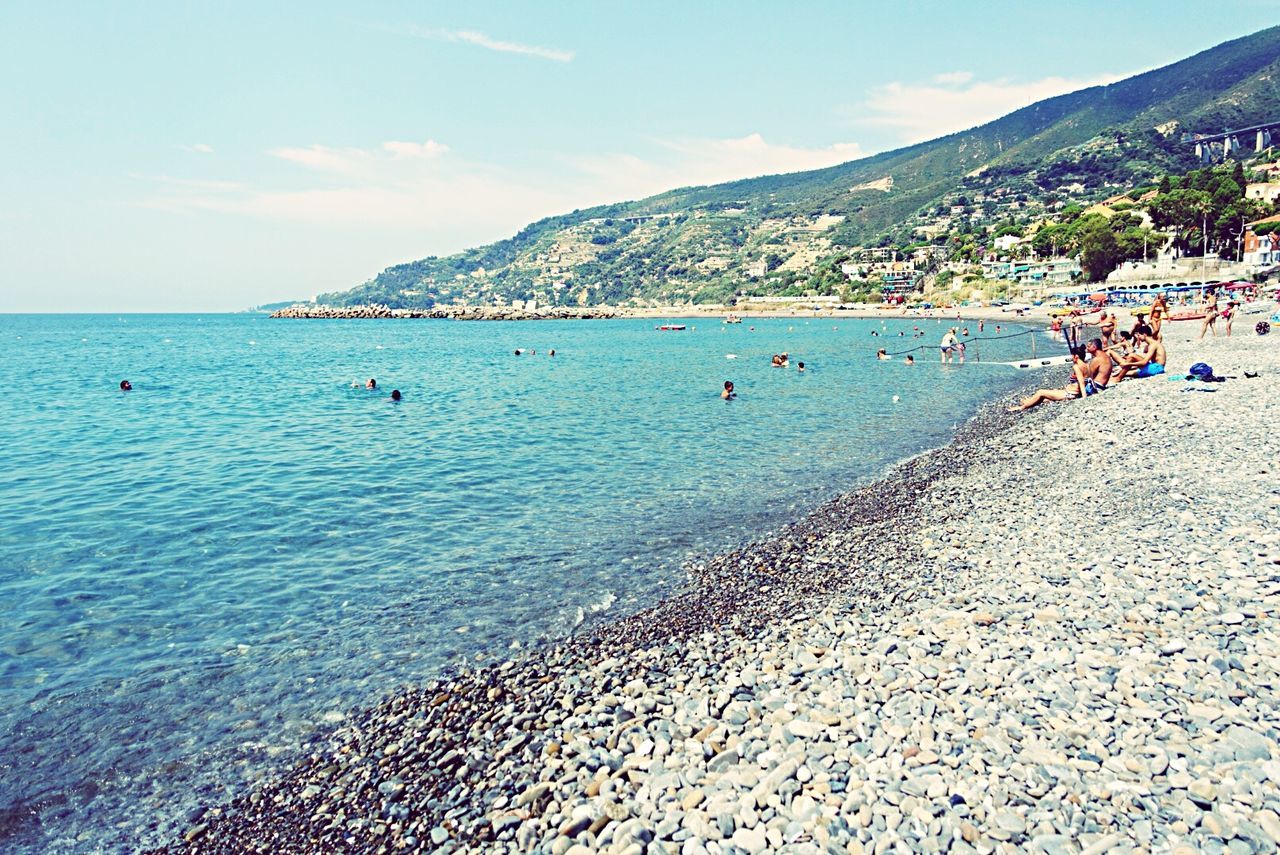 sea, water, beach, mountain, sky, shore, sand, scenics, large group of people, vacations, beauty in nature, incidental people, tranquil scene, nature, tranquility, coastline, tourist, day, leisure activity