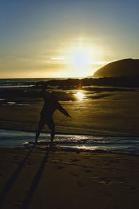 Silhouette man standing on beach against sky during sunset