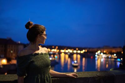Woman looking at illuminated city against sky during night