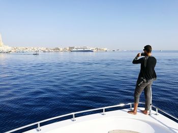 Rear view of woman photographing sea against clear sky