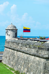 Colombian flag on castle by sea against blue sky during sunny day
