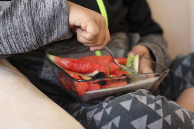 Midsection of boy eating fruits while sitting on sofa at home