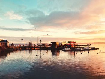 Silhouette boats moored at harbor against sky during sunset