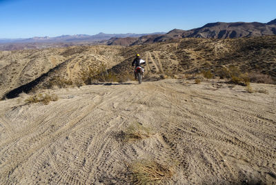 Rear view of man  riding into desert hills on dirt bike