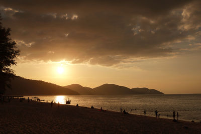 Silhouette people on beach against sky during sunset