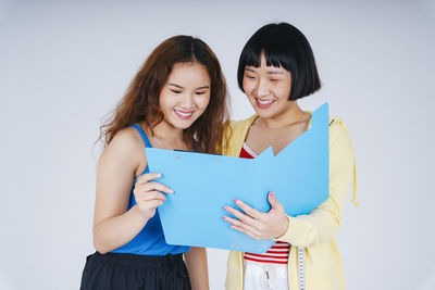 Smiling lesbian couple looking at file against gray background