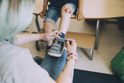 High angle view of female teacher helping boy in wearing shoe at preschool