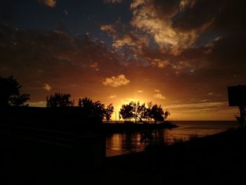 Silhouette trees by lake against sky during sunset