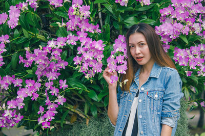 Portrait of beautiful young woman standing by purple flowering plants