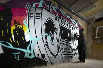 Rear view of man standing against graffiti wall