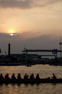 Silhouette people on bridge over river against sky during sunset