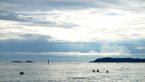 Silhouette people swimming in sea against cloudy sky