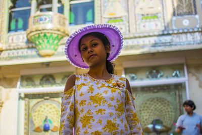 Portrait of woman wearing hat standing against built structure