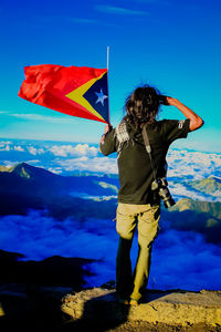 Rear view of hiker holding flag while standing on mountain