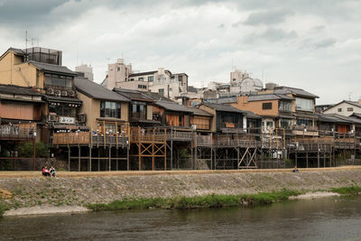 Buildings by river against cloudy sky