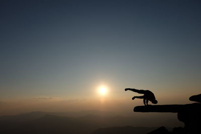 Silhouette man doing handstand on mountain against sky during sunset