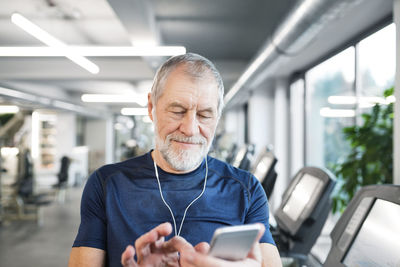 Senior man with smartphone and earphones in gym