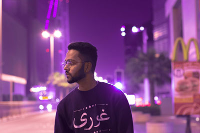 Portrait of young man standing against illuminated light at night