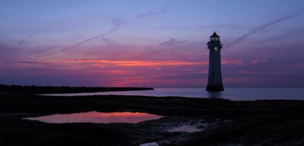 Lighthouse by sea against sky during sunset