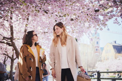 Smiling young women walking under cherry blossom