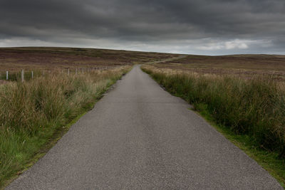 Empty road amidst field against sky