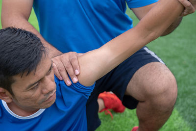 Low section of male physical therapist stretching soccer player hand on field