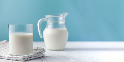 A jug and a glass of fresh milk on a blue background.