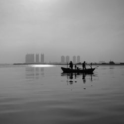 Silhouette people on boat sailing in sea against sky