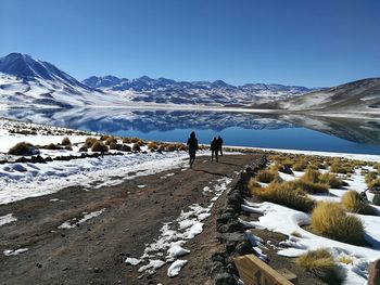 Rear view of people walking on road by lake against clear sky