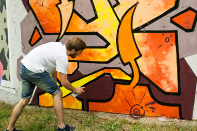 Young man spray painting wall in city