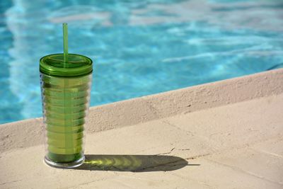 Close-up of water glass with straw beside swimming pool