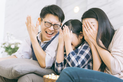 Smiling parents with daughter covering faces in living room at home