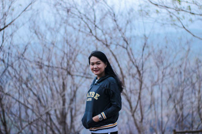 Portrait of smiling woman standing against bare trees