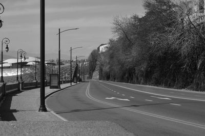 Empty road by trees in city against sky