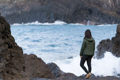 Rear view of woman standing on rock by sea