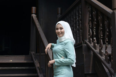 Portrait of smiling young woman standing against railing