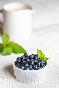 Bowl with forest blueberries and white milk jug with milk on white wooden background.