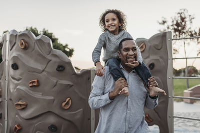 Joyful son sitting on a happy father's shoulders at park playground