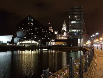 Illuminated buildings by river against sky at night